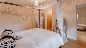 Une chambre à coucher avec un lit à baldaquin, une table de chevet, un miroir et une salle de bain visible à travers une porte ouverte.