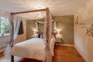 A four-poster canopy bed with a lace canopy, bedside lamps, and a wall with a floral design. - Willow Lodge, Hot Tub, Woodburner (Exeter)