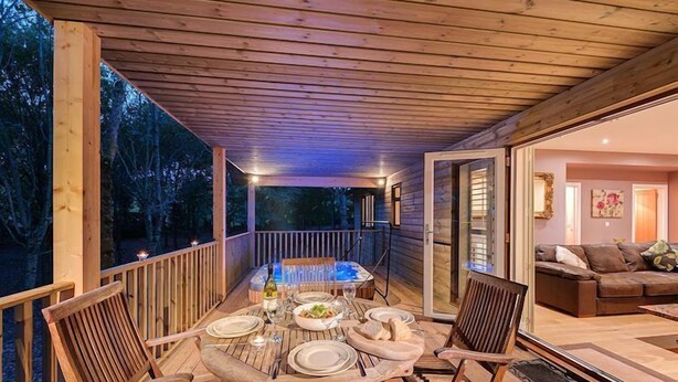Une terrasse extérieure en bois, avec une table à manger pour quatre personnes, entourée de chaises.