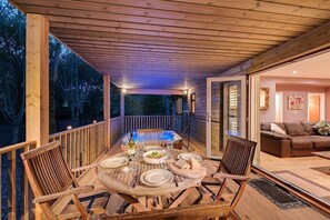 Une terrasse extérieure en bois, avec une table à manger pour quatre personnes, entourée de chaises.