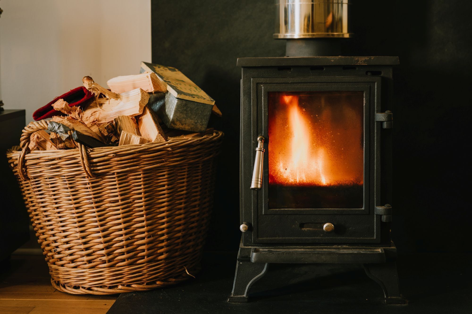 A wood-burning stove with a basket of firewood beside it.