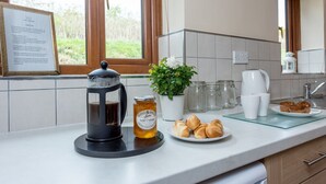 Eine Küchenarbeitsplatte mit einer French Press, einem Marmeladenglas mit Orangen- und Mandarinenmarmelade, einer Topfpflanze und einem Teller Croissants.