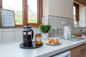 Keittiön työtasolla on pressopannu, purkki appelsiini-mandariinimarmeladia, ruukkukasvi ja lautanen täynnä croissantteja.