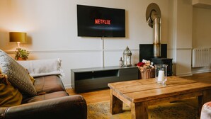 Ein Wohnzimmer mit einer Ledersofa, einem Holztisch, einem an der Wand montierten Fernseher, einem Kamin und einer Lampe.
