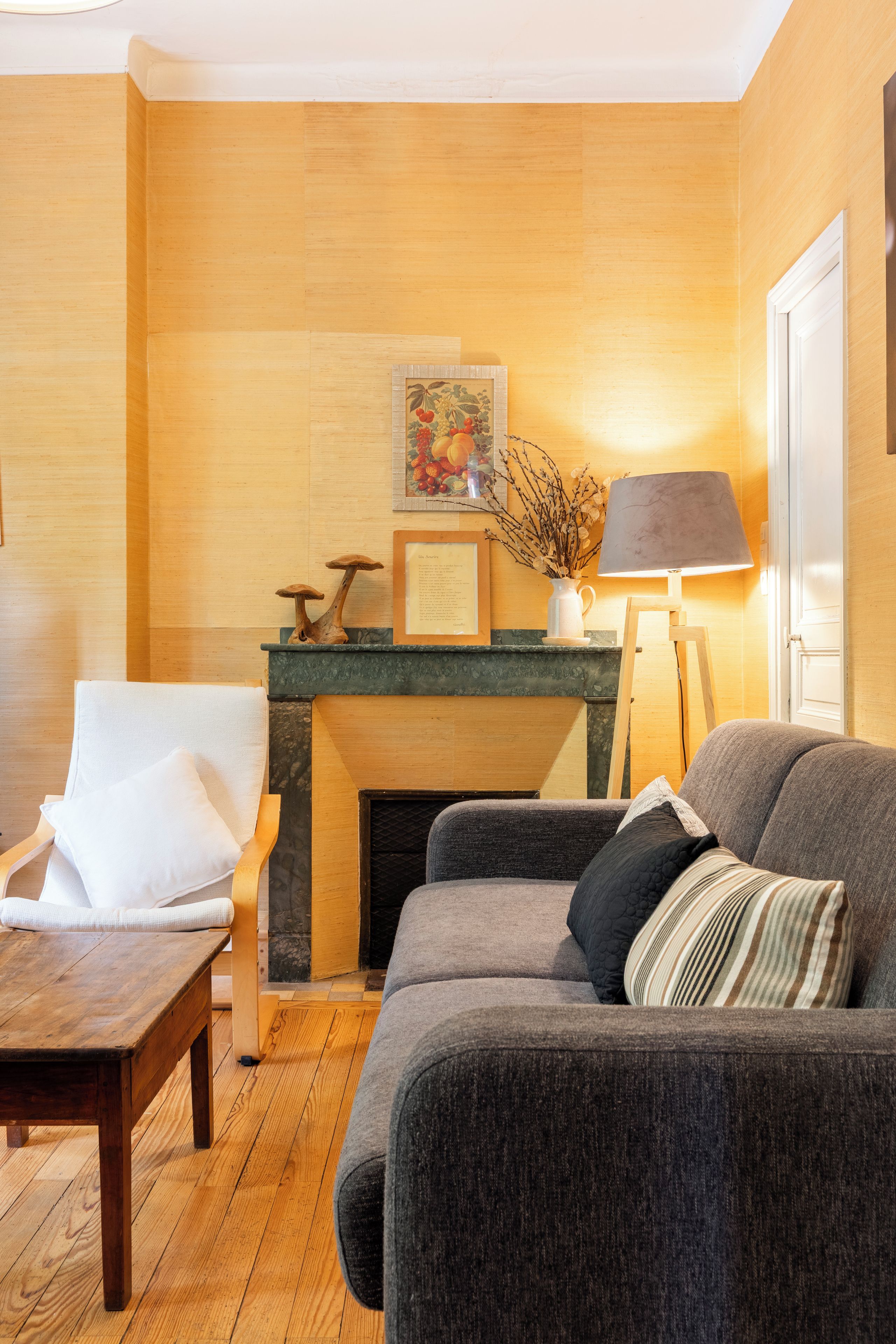 A cozy living room with a fireplace, a sofa, a chair, and a lamp.