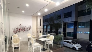 A modern indoor seating area with white chairs and tables, a decorative branch sculpture, and a view of the street at night. - Dyn Opera Hotel (Ho Chi Minh City)