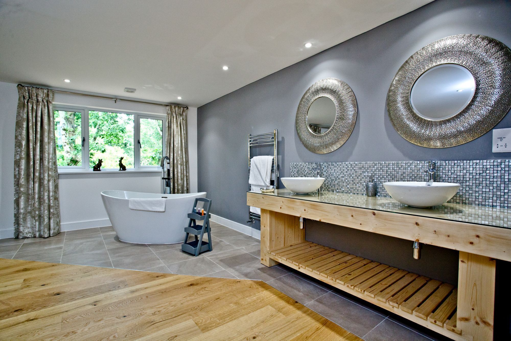 A modern bathroom with a freestanding bathtub, two sinks, and decorative mirrors.