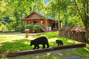 A cabin with a porch, surrounded by a stone wall and a grassy yard. - Cozy Bear, Free Attraction Tickets, Hot Tub, WIFI, Fireplace!!! (Sevierville)