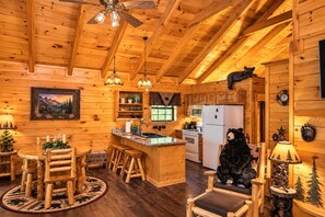 A cabin interior with a wooden interior, a dining area, kitchen, and a bear statue.