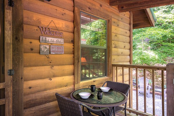 A wooden cabin with a welcome sign, a window with a view of trees, and a table with chairs and bowls. - Cozy Bear, Free Attraction Tickets, Hot Tub, WIFI, Fireplace!!! (Sevierville)