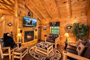 A cozy log cabin interior with a fireplace, wooden furniture, a television, and a bear-themed decor.