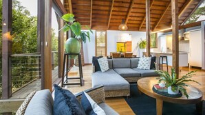 A spacious living area with a wooden ceiling, a grey sectional sofa, a round coffee table, and a dining table with chairs. - Hepburn Spa Pavilions (Hepburn Springs)