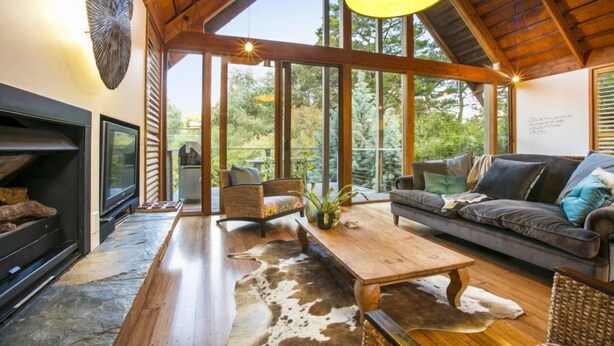 A spacious living room with a fireplace, large windows, and a high ceiling. - Hepburn Spa Pavilions (Hepburn Springs)