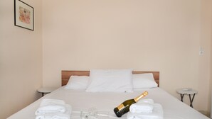 A neatly made bed with white linens, a bottle of champagne, and a glass on the bed.