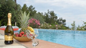 A bottle of Villa Sandi Prosecco, a bowl of strawberries, a pineapple, and a glass of wine by a poolside.