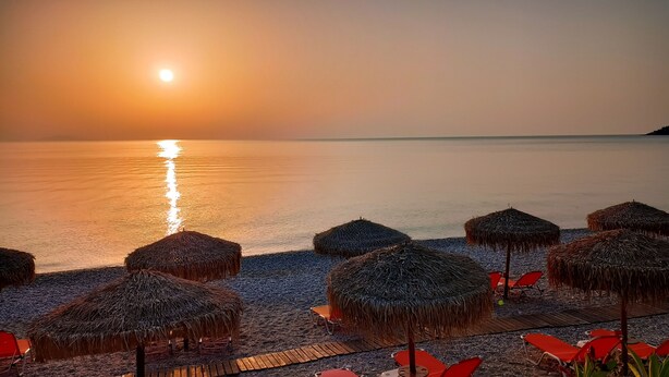 A beach with thatched umbrellas and red lounge chairs.