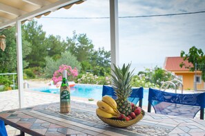 Una mesa con una botella, un cuenco de fruta y una piscina al fondo.