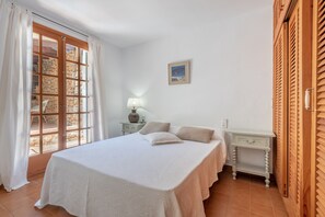 A bedroom with a bed, a nightstand, a lamp, a painting, and a wooden wardrobe.