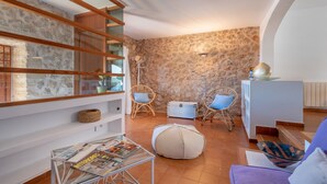 Una sala de estar acogedora con pared de piedra, vigas de madera, sillones de mimbre, una mesa de vidrio y un sofá.