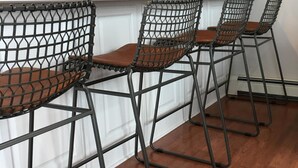 Una cocina con armarios blancos, un refrigerador blanco, un lavamanos y tres taburetes de estructura metálica negra con cojines marrones.