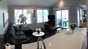 Una cocina moderna con estufa integrada, cafetera y hervidor. Hay una zona de comedor con una mesa redonda y sillas.