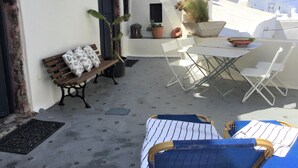 Un patio con un banco de madera, sillas blancas y una mesa.