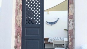 Un edificio blanco con una puerta negra, una banca y una mesa con sillas afuera.