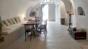 Una habitación acogedora con paredes blancas, un comedor con mesa y sillas de madera, un sofá con cojines estampados y un televisor montado en la pared.