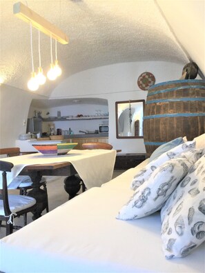 A cozy room with a bed, a dining table, and a kitchen area in the background.