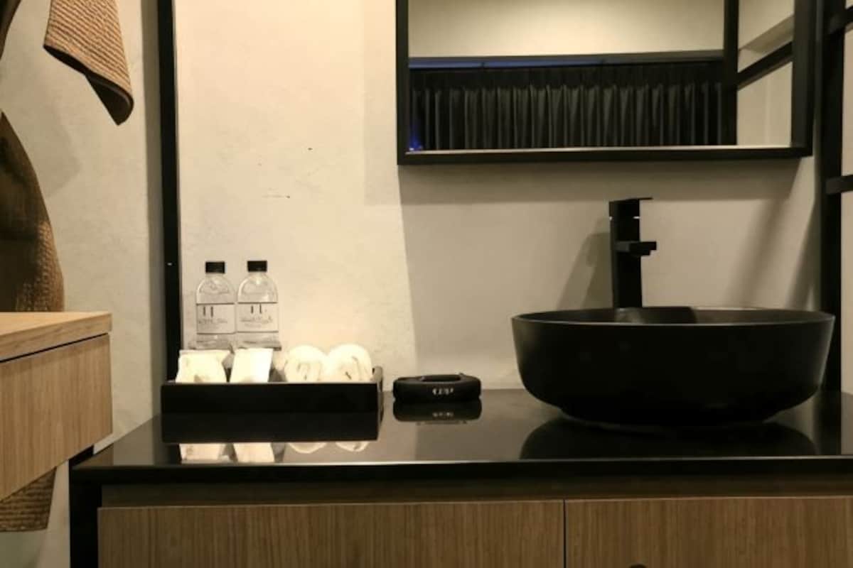 A modern bathroom with a black sink, a mirror, and a towel rack with bottles and tissues.