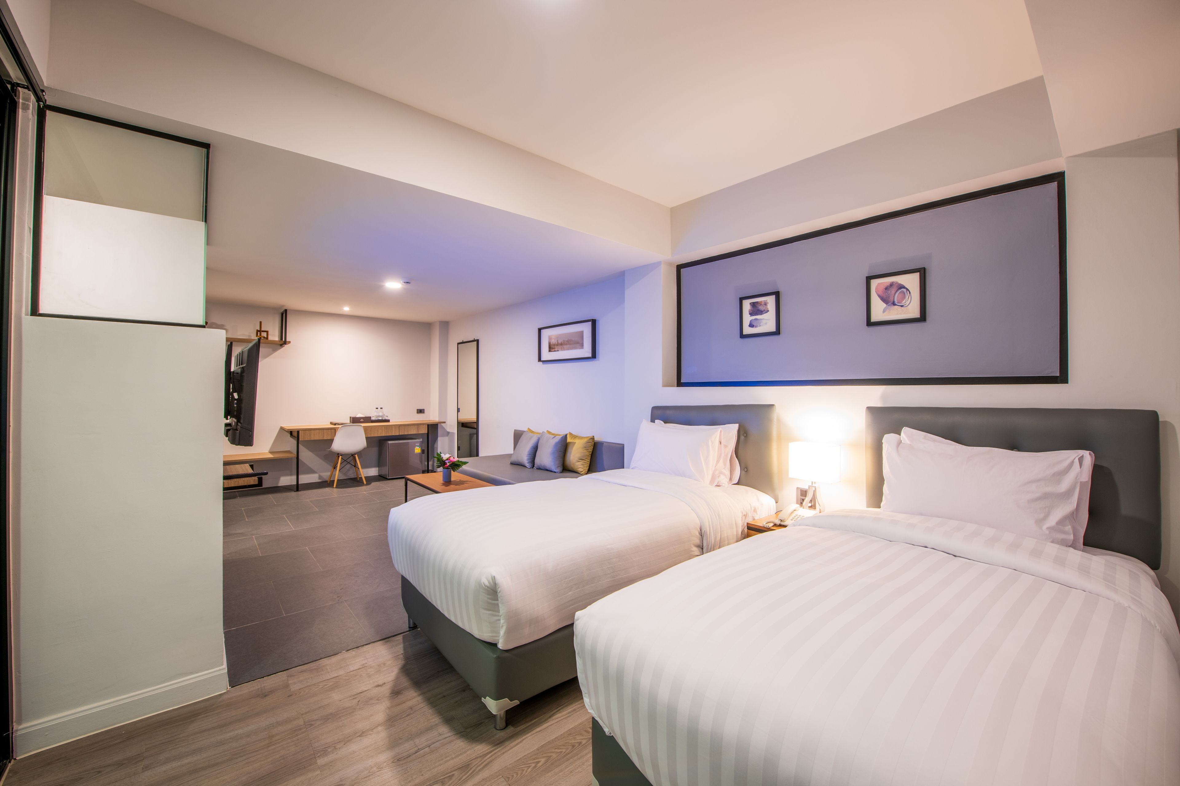 A hotel room with two beds, a desk, and a seating area.
