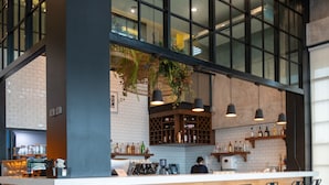 A modern bar area with a high ceiling, large windows, and a bar counter with stools. - Mayson Place (Samut Prakan)