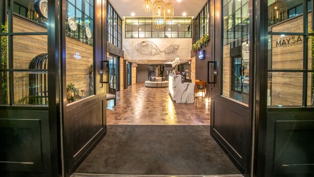 A modern hotel lobby with a reception desk, a large chandelier, and a view of the city through floor-to-ceiling windows. - Mayson Place (Samut Prakan)