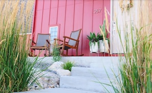 Welcome to a charming entrance with a cozy outdoor seating area, complete with a wooden rocking chair and wicker chair.