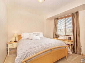 Relax in this cozy hotel room featuring a large bed, nightstand, and window with a view.