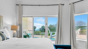 Ett hotellrum med en stor säng, en sänglampa, utsikt över en balkong med en pool och en stol.