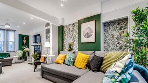 Una sala moderna con un sofá seccional gris, paredes de acento verde y papel tapiz tropical.