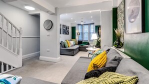 Una sala de estar moderna con un sofá gris, una escalera y una pared de acento verde.