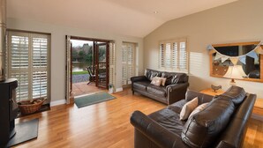 A spacious living room with a leather sofa, a television, and a large window with blinds. - Heron Lodge, Hot Tub, Woodburner (Exeter)