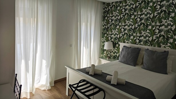 A hotel room with a bed, a desk, a chair, and a window with sheer curtains.