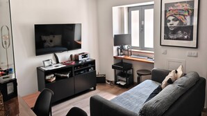 A modern living room with a flat-screen TV, a desk with a computer, and a large framed artwork on the wall.
