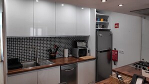 A modern kitchen with white cabinets, a black and white backsplash, a stainless steel sink, a microwave, a refrigerator, and a wooden countertop.