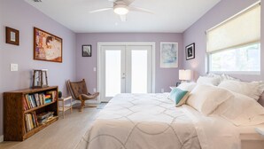 Un dormitorio con una cama, una estantería, una silla y un ventilador de techo.