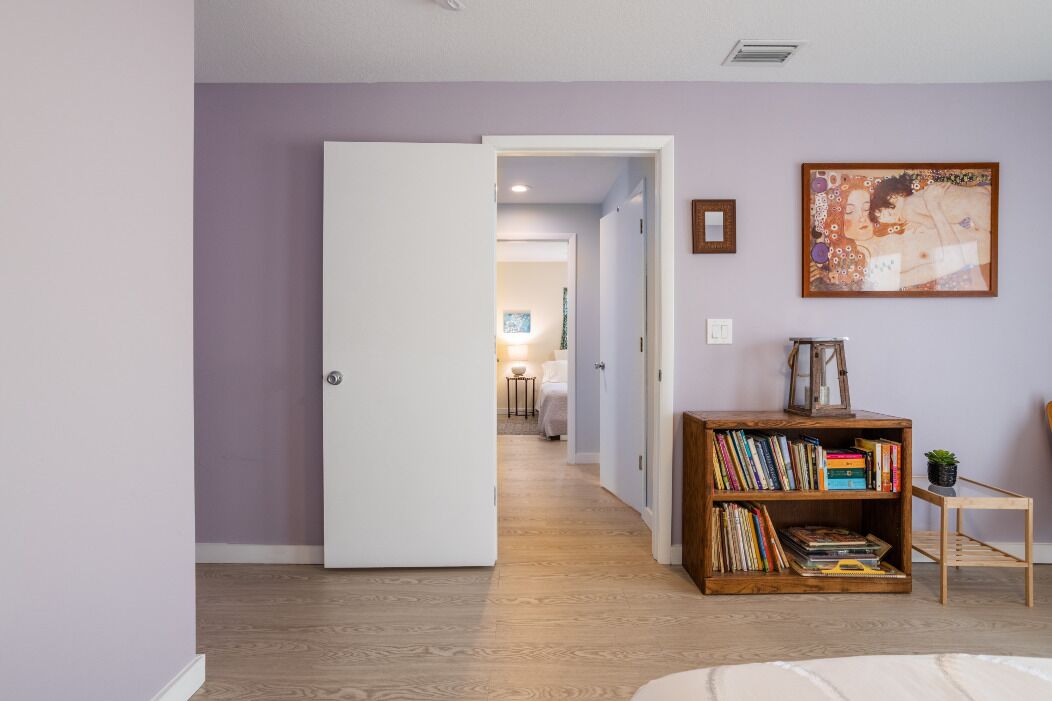 Un pasillo con una puerta blanca que da a un dormitorio, una estantería llena de libros y un cuadro en la pared.