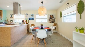 Una cocina moderna con una isla central, iluminación colgante y un comedor con sillas y una mesa.