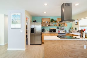 Una cocina moderna con un refrigerador de acero inoxidable, un microondas y un horno empotrado. Hay una isla de madera con un lavamanos y una campana extractora grande sobre la estufa.