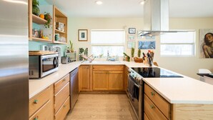 Una cocina moderna con armarios de madera, un refrigerador de acero inoxidable, un microondas y un horno. Hay repisas de madera con plantas y utensilios de cocina.