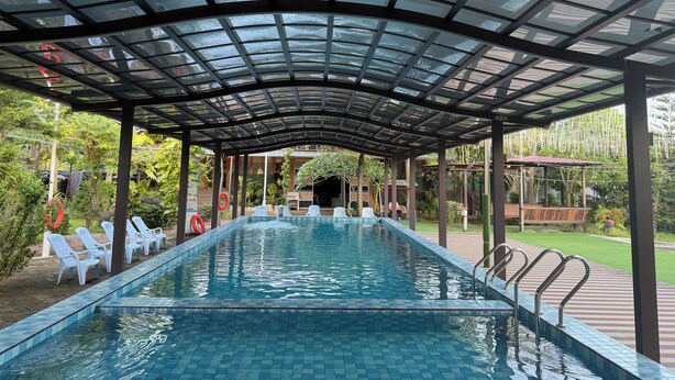 Una piscina techada con agua azul cristalina, rodeada de sillas de descanso blancas y una estructura de techo de vidrio.