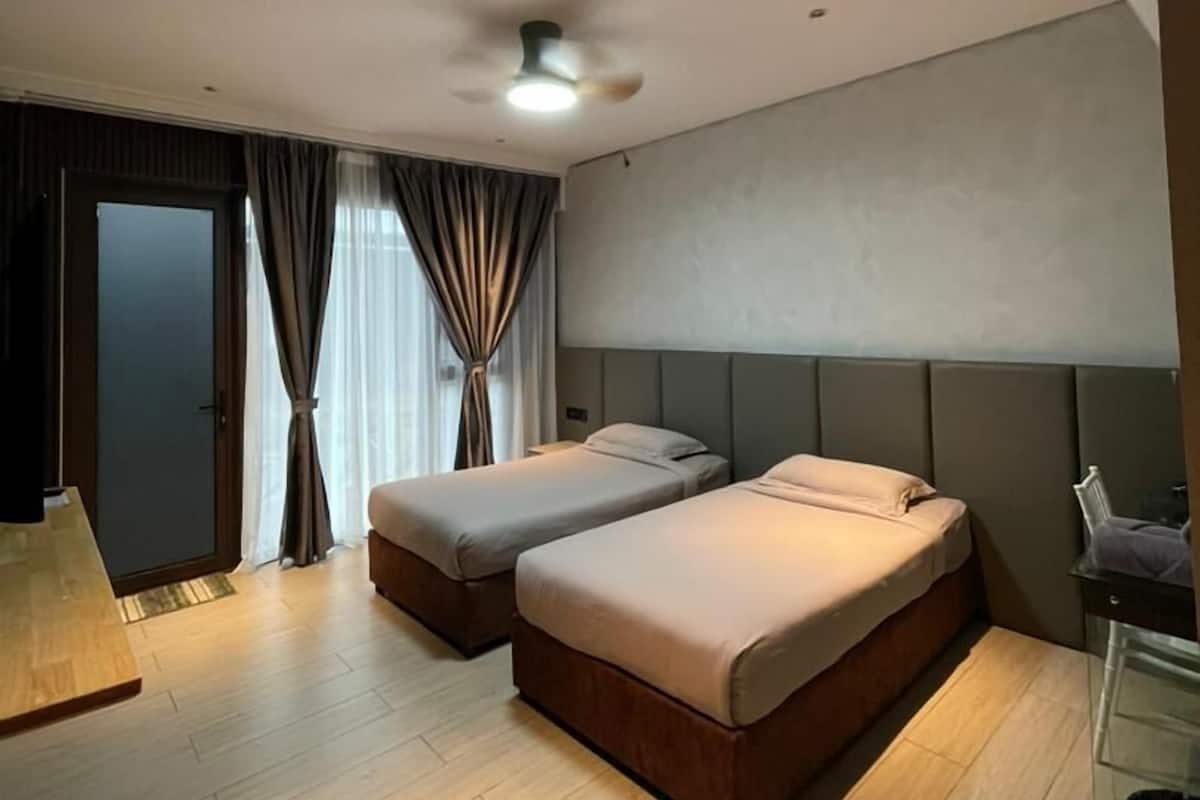 A modern hotel room with two beds, a ceiling fan, a large window with curtains, and a wooden floor.
