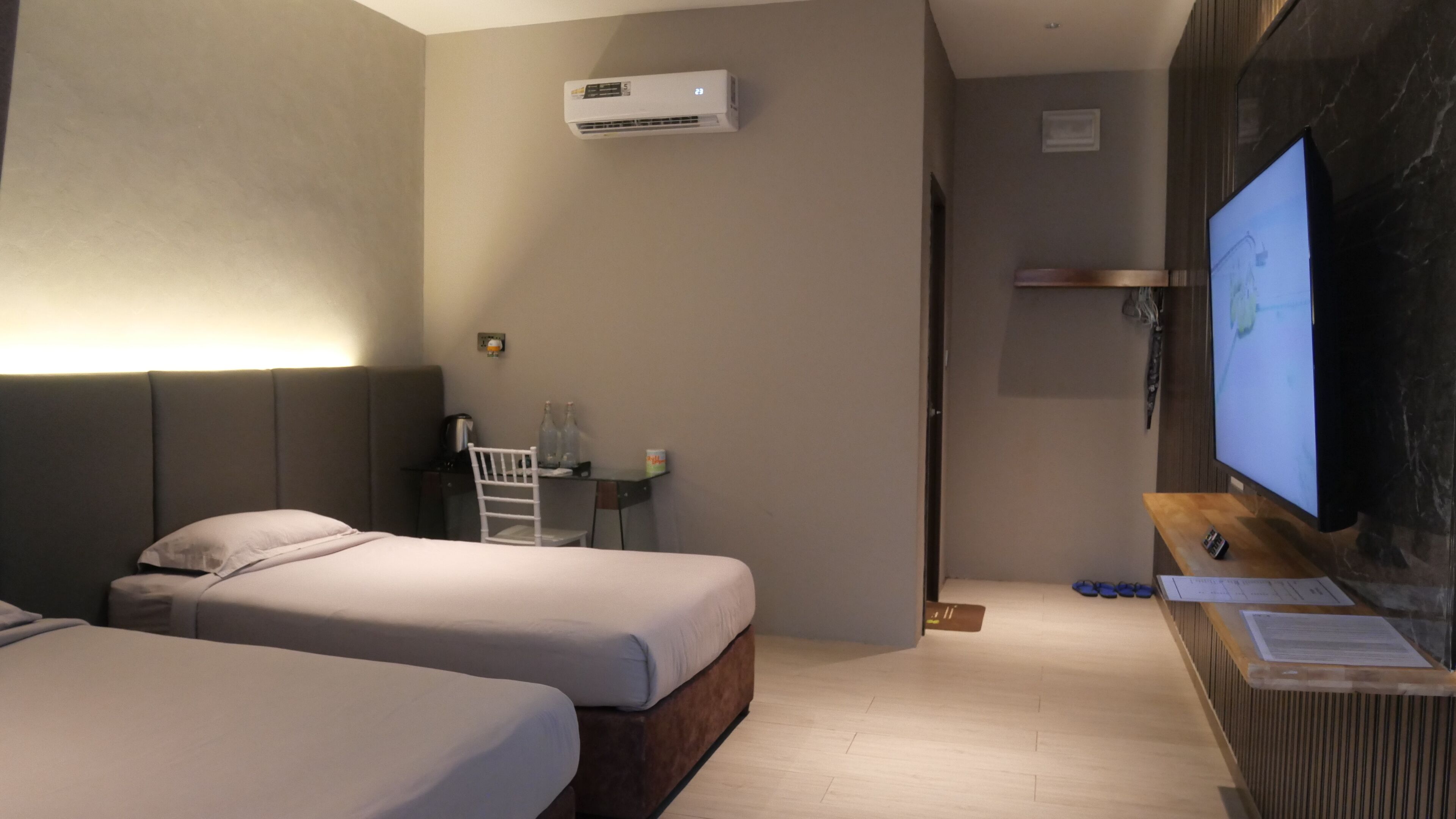 Habitación de hotel con dos camas, un escritorio con silla, televisor y aire acondicionado.